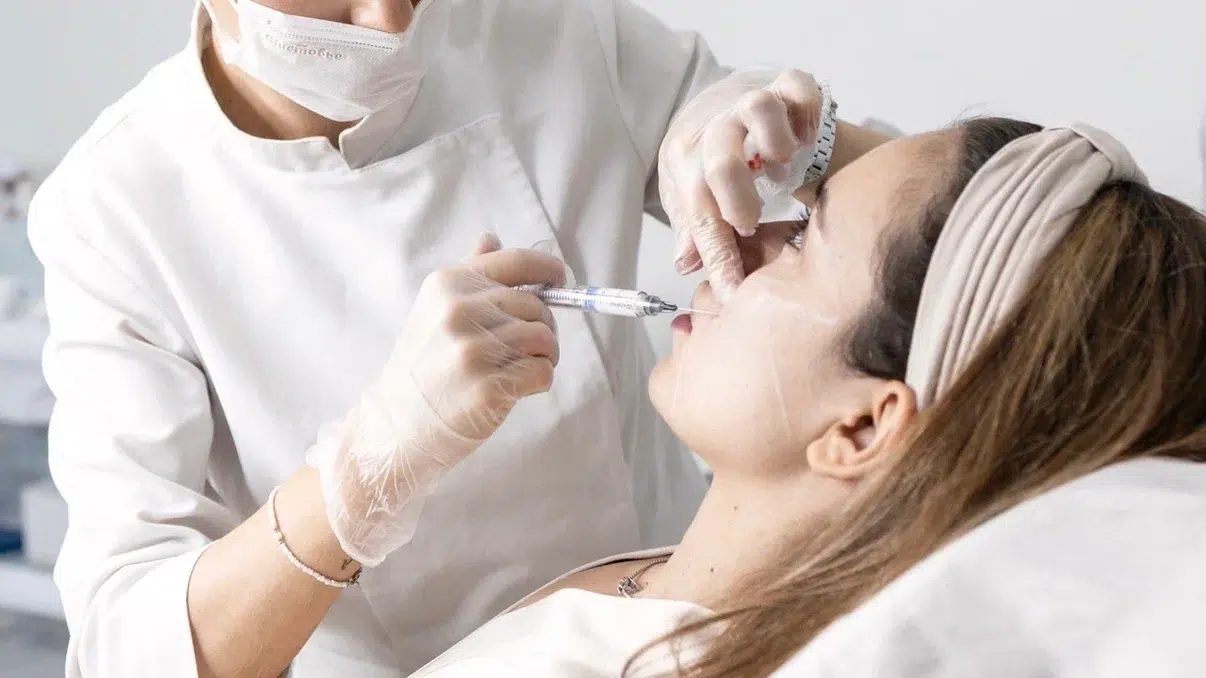 Doctor in gloves and a mask injecting along the upper lip of a patient lying in a treatment chair